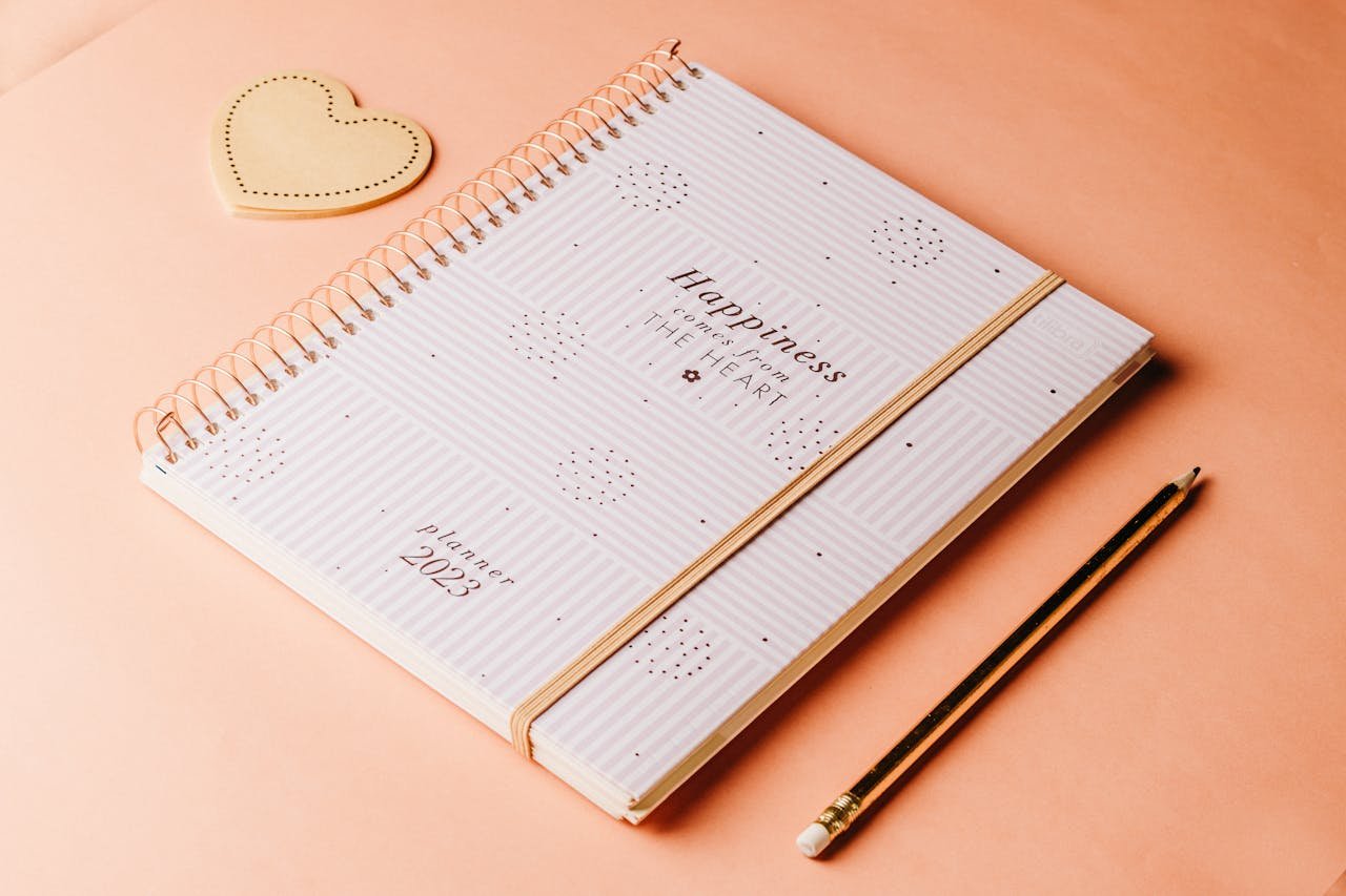 Stylish planner and pencil set on a peach textured backdrop.
